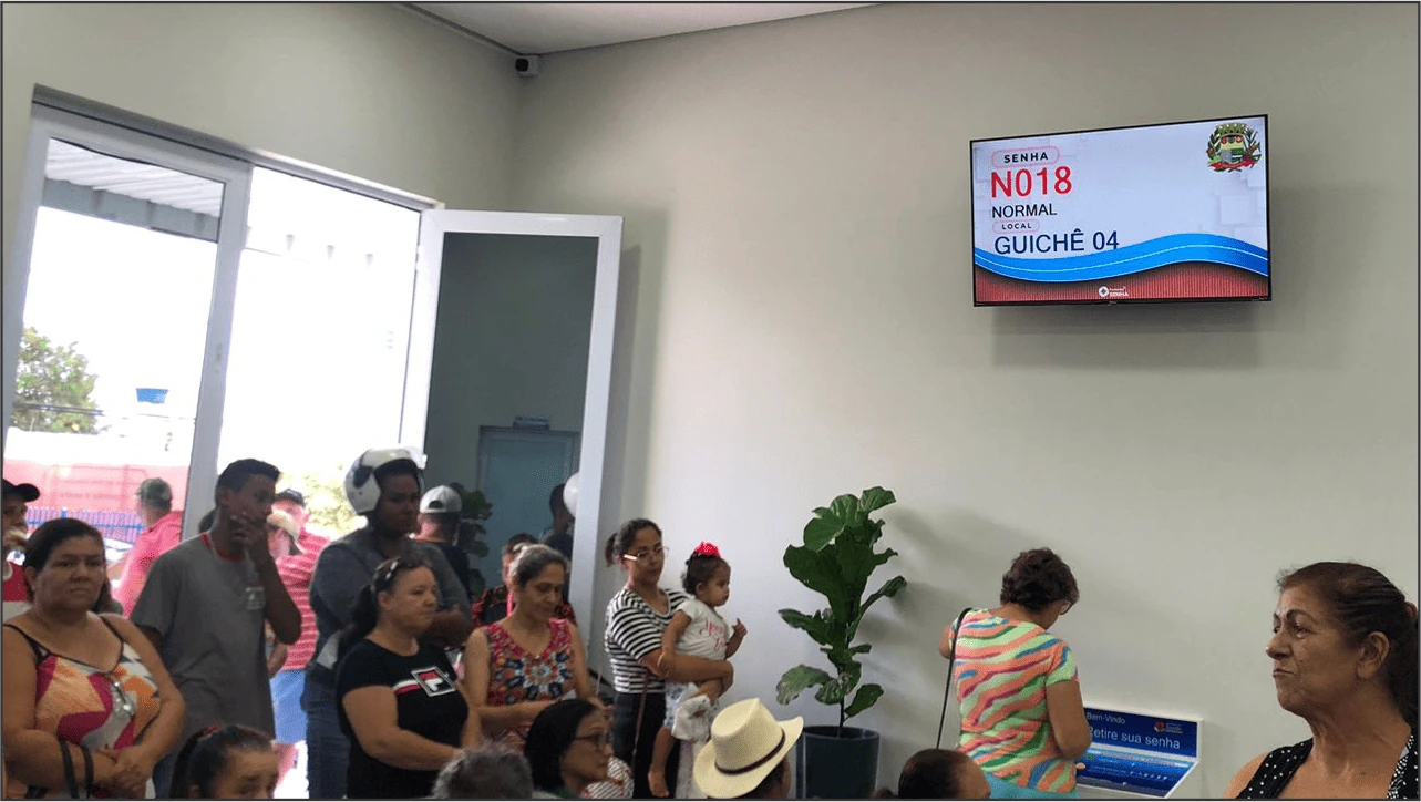 Ambiente de saúde com televisão chamando senha e autoatendimento