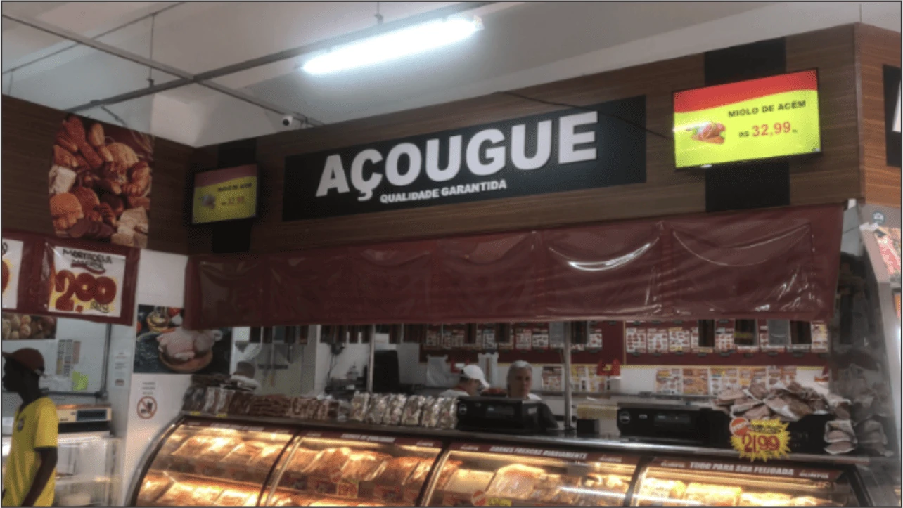 Açougue com duas televisões exibindo promoções de carnes