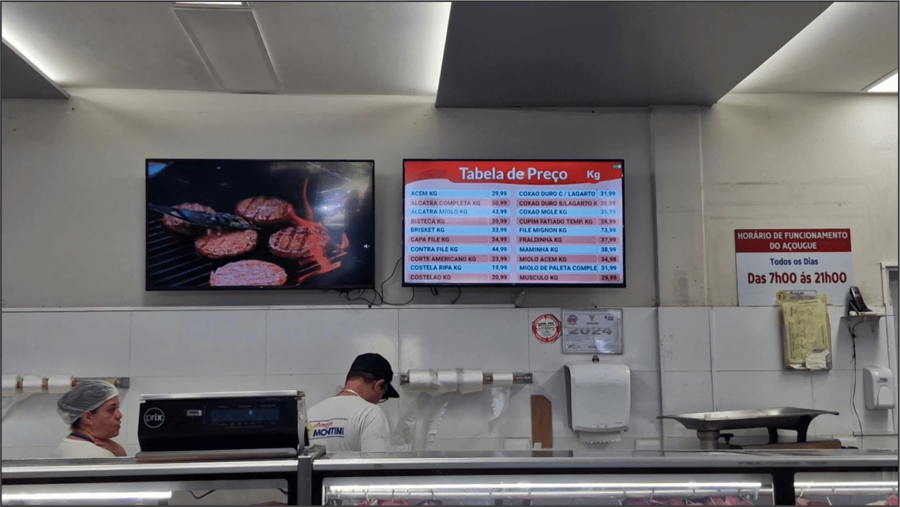 Açougue com dois televisores: um com conteúdo de mídia e outro com tabela de preços